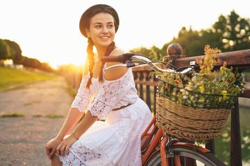 Young beautiful woman sitting on her bicycle with flowers at sunset