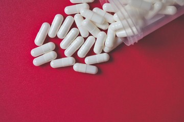 Close up of white pills or capsules spilling out of bottle or container, medical background, medication or drug therapy concept 