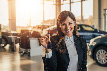 Cheerful young woman showing her new car key at dealership.