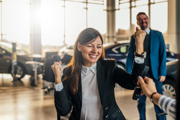 Fototapeta na wymiar Cheerful young woman receiving the keys of her new car at car dealership.