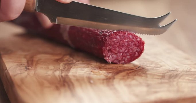 Slow motion closeup female slicing thin salami sausage