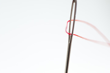 Needle eye close up shot , red thread, isolated on white background.