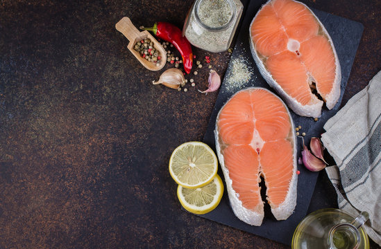 Two fresh raw salmon steaks on slate board with salt, peppers, lemon on dark table background, top view. Healthy Dieting Food Concept