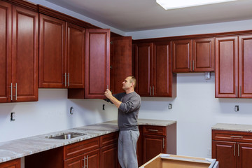 The worker sets a new handle on the white cabinet with a screwdriver