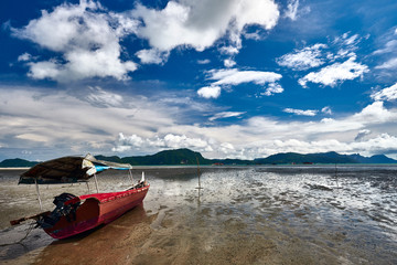 The sea tide with a old colorful asian fishing boats and dramatic sky on the background. Langkawi island, Malaysia.