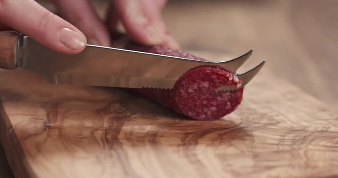 Slow motion closeup female slicing thin salami sausage