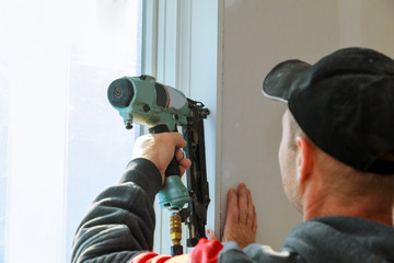 Carpenter using brad nail gun complete trim window