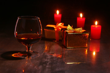 christmas decoration. glass of cognac or whiskey, red candles and gift box on a wooden background.