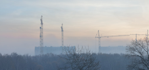 Construction cranes in the morning fog