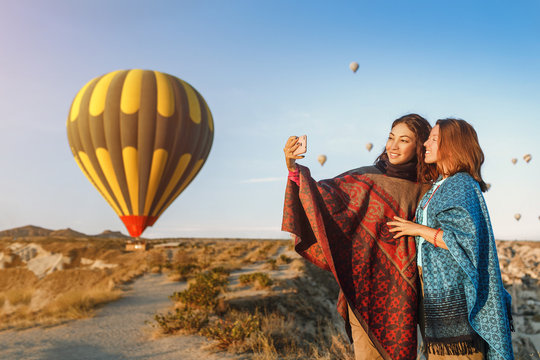 Couple of friends travelers enjoying valley view and making selfie on a phone with wonderful balloons flight over Cappadocia valley in Turkey