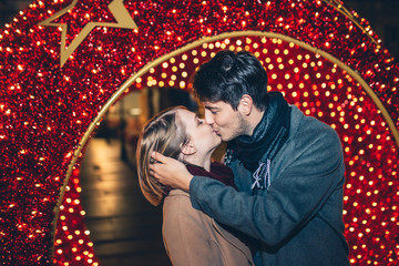Beautiful young couple in love enjoying Christmas or New Year night on a city street. 
