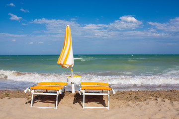 Adriatic Sea coast view. Seashore of Italy, summer umbrellas on sandy beach with clouds on horizon.