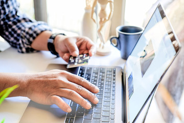 Online payment concept : Man's hand holding credit card while using computer laptop for online shopping or paying a bills.