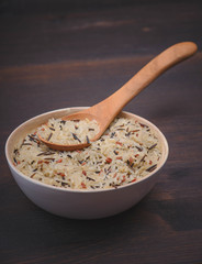 whole grain mix rice in the white bowl with wood spoon on the dark table