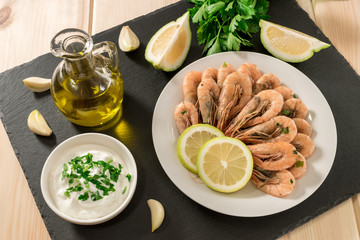 Seafood. Shrimps with fresh herbs, olive oil, sauce and lemon on white plate on wooden light background