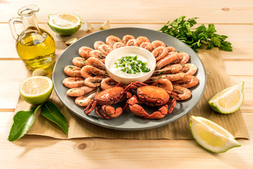 Cooked shrimps and crabs served on wooden light background with lemon, sauce and garlic close up