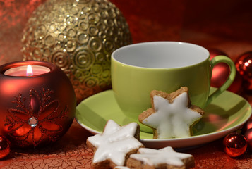 A green cup with star-shaped cinnamon biscuits and a red Christmas ball candle