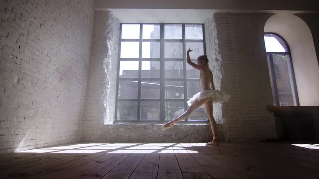 Female ballet dancer training in loft style studio in front of big window