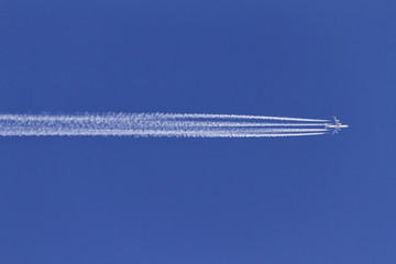 Airplane leaving condensation trails on a clear blue sky.