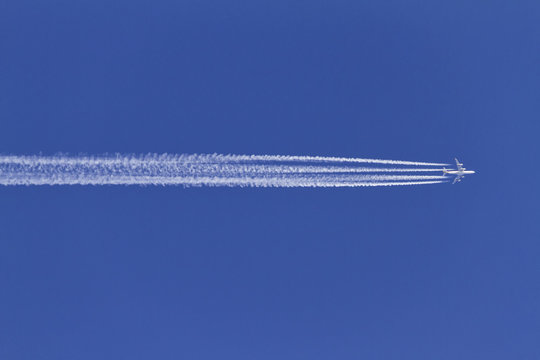 Airplane leaving condensation trails on a clear blue sky.