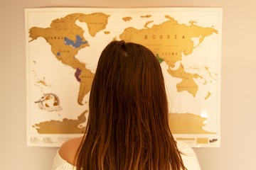 Teenage girl looking at a destination on a scratch map of the world on the wall