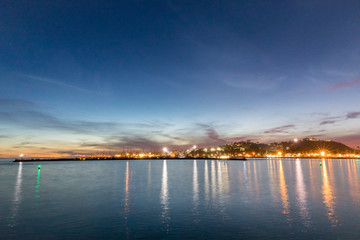 Beautiful night view from the shore over water to a city lights reflected on water in evening