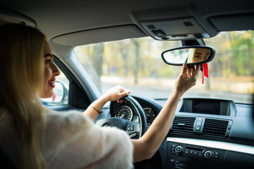 Happy young woman driver looking adjusting rear view car mirror, making sure line is free visibility is good before making turn. Safe trip, journey driving concept