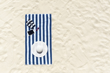 Top view of sandy beach with towel frame and summer accessories. Background with copy space and visible sand texture.
