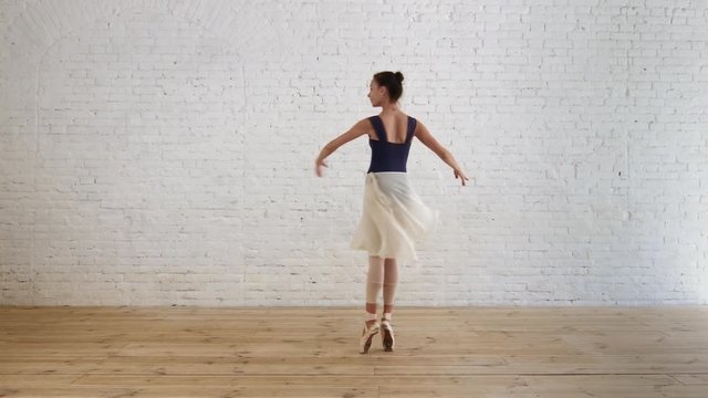 Ballerina performs pirouette in room on the brick wall background