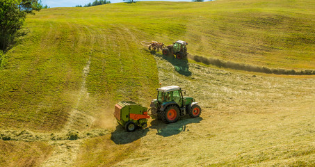 Haymaking on a hillside with rows of hay, a hay tedder and a hay-loader