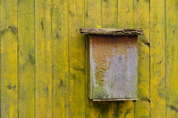 The old plywood mailbox is on a yellow fence. The paint on the mailbox and the fence peeled off. Background. Texture.