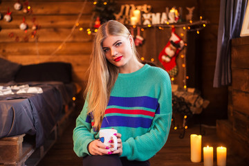 Attractive young woman with a cup of coffee or tea in her hands in a christmas interior