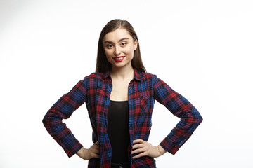 Studio shot of attractive self confident young female in great mood feeling happy, holding hands on her slender waist and looking at camera with radiant smile, rejoicing at good day or news