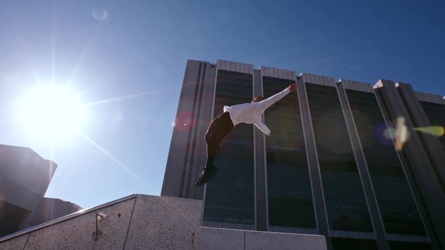 Man practices parkour and free running by doing a back flip from a wall outdoors. Young man practicing extreme sport outdoors in city.