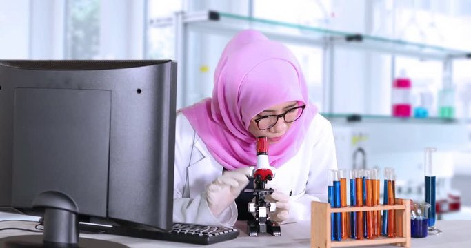 Female researcher working with a computer and microscope in the laboratory, shot in 4k resolution