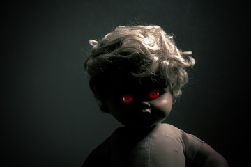 Creepy doll with red glowing eyes in the dark 