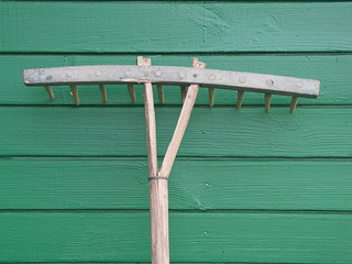old wooden rake on a green background of boards
