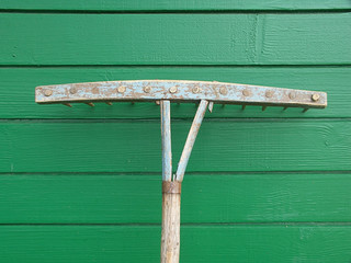 old wooden rake on a green background of boards