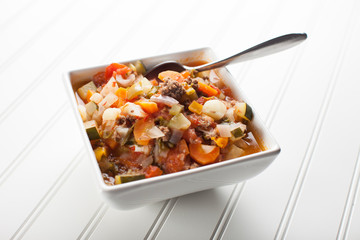 
Homemade gumbo soup with cooked sausage, onion, carrots, zucchini, tomatoes, and potatoes in white bowl full view shot
