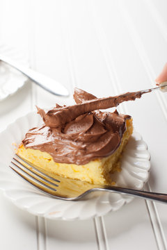 
Chocolate Frosting With A Slice Of Yellow Cake On White Background Being Spread
