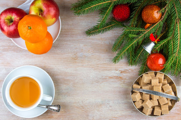 A cup of tea, a teapot and a plate of fruit on a rustic wooden background with branches of a Christmas tree and Christmas toys, copy space.