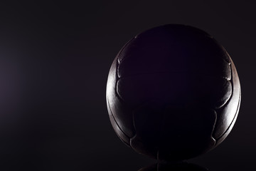 Fototapeta na wymiar Old football leather ball on a black background