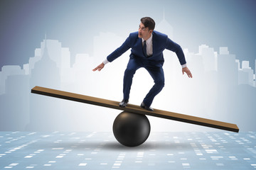 Businessman trying to balance on ball and seesaw