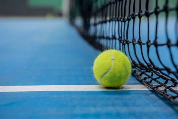 Rolgordijnen Yellow tennis ball on blue hard court surface with black net © ivananikolic