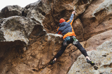 Hipster - climber at the age of climbing up a beautiful rock without insurance and helmet