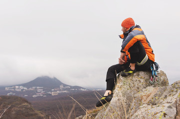 Hipster - a climber in a down jacket and a knitted cap sits and rests on the top of a rock