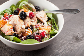
Freshly made green spinach salad with raspberries, orange slices, boysenberries, and feta cheese in white bowl close up shot
