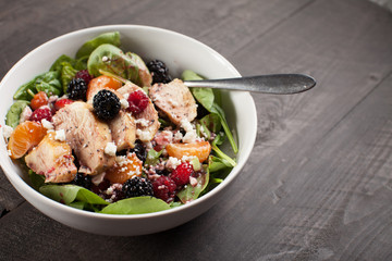
Freshly made green spinach salad with raspberries, orange slices, boysenberries, and feta cheese in white bowl horizontal shot 
