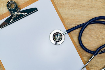 Stethoscope and clipboard with blank white paper sheet on wood table top view with copy space. health concept.