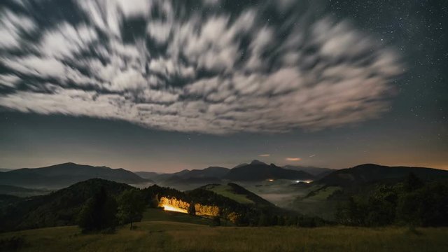 Stars moving in night sky over mountains and foggy rural landscape at moonlight. Night to day time lapse dolly shot